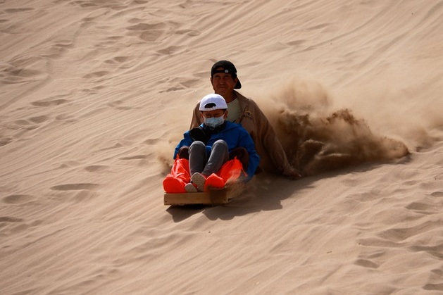 2021年5月3日，游客在甘肃省敦煌市鸣沙山月牙泉景区滑沙。