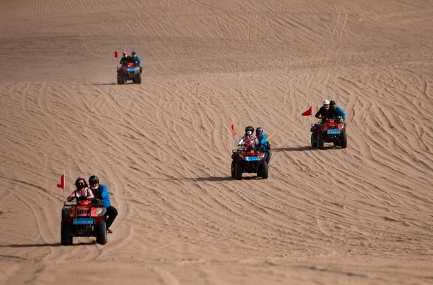 2021年5月3日，游客在甘肃省敦煌市鸣沙山月牙泉景区乘坐沙漠越野摩托车游玩。