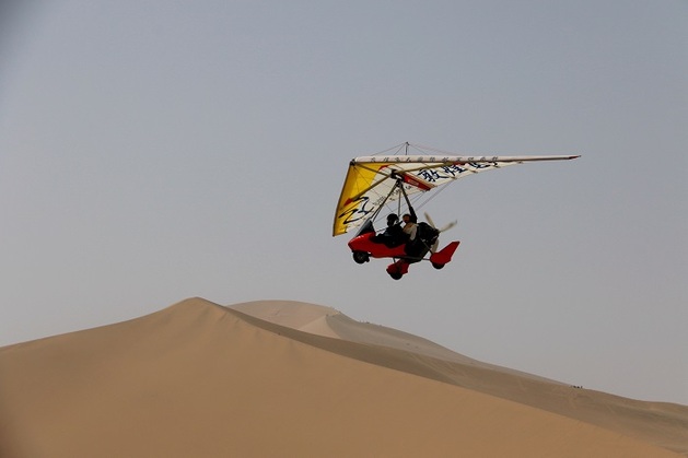 2021年5月3日，游客在甘肃省敦煌市鸣沙山月牙泉景区乘坐动力滑翔机欣赏大漠风光。