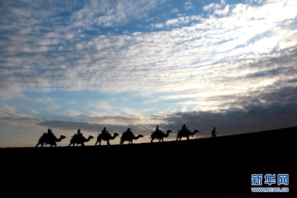 5月15日，游客骑骆驼在甘肃省敦煌市鸣沙山月牙泉景区游览。晨光下，云彩、沙山、驼队构成了一幅美丽迷人的画卷。新华社发（张晓亮 摄）