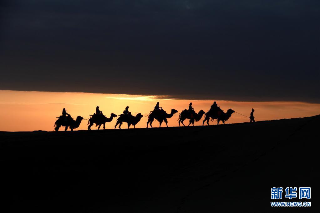 5月15日，游客骑骆驼在甘肃省敦煌市鸣沙山月牙泉景区游览。晨光下，云彩、沙山、驼队构成了一幅美丽迷人的画卷。新华社发（张晓亮 摄）