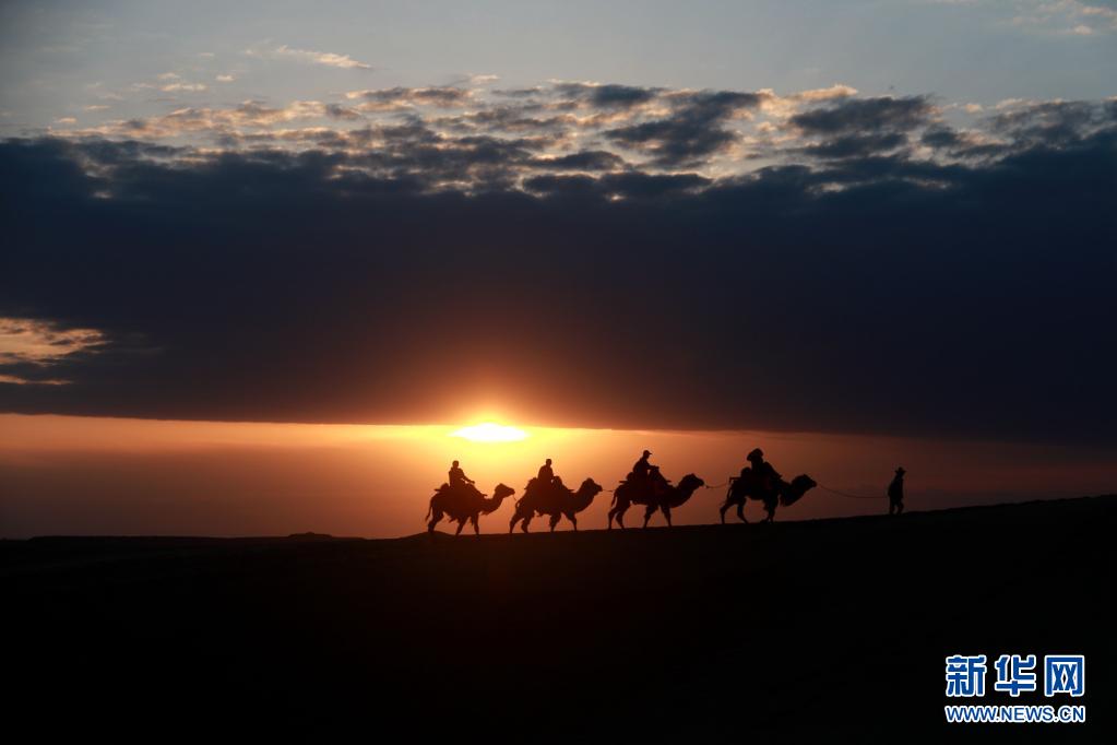 5月15日，游客骑骆驼在甘肃省敦煌市鸣沙山月牙泉景区游览。晨光下，云彩、沙山、驼队构成了一幅美丽迷人的画卷。新华社发（张晓亮 摄）