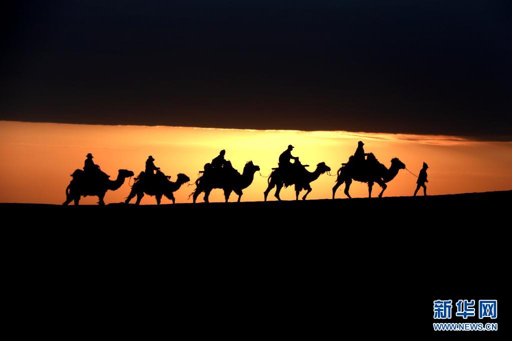 5月15日，游客骑骆驼在甘肃省敦煌市鸣沙山月牙泉景区游览。晨光下，云彩、沙山、驼队构成了一幅美丽迷人的画卷。新华社发（张晓亮 摄）