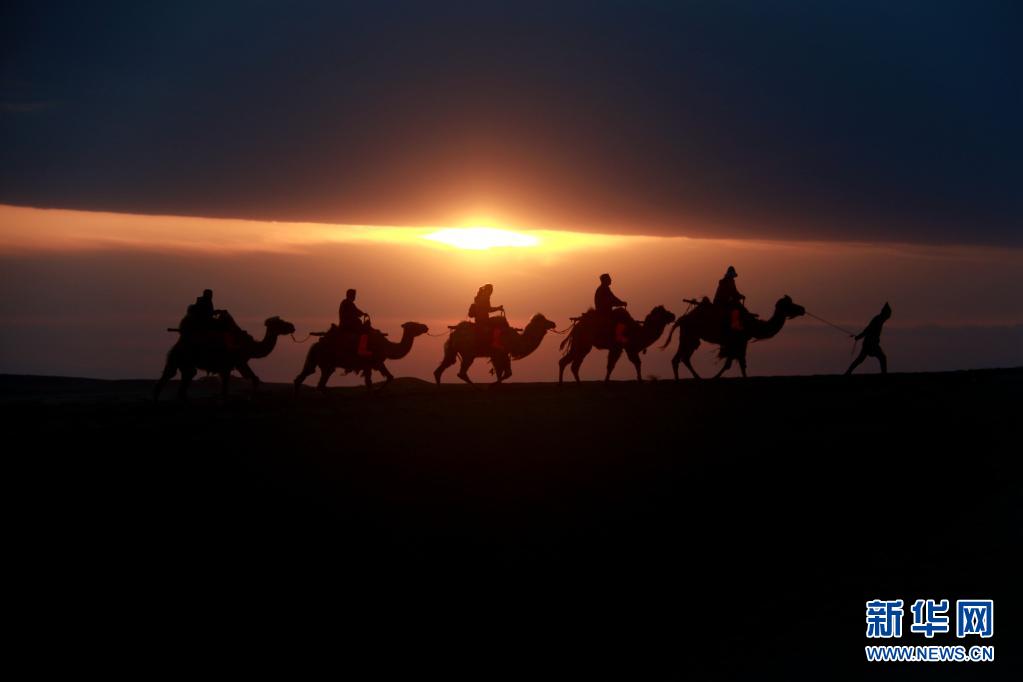 5月15日，游客骑骆驼在甘肃省敦煌市鸣沙山月牙泉景区游览。晨光下，云彩、沙山、驼队构成了一幅美丽迷人的画卷。新华社发（张晓亮 摄）