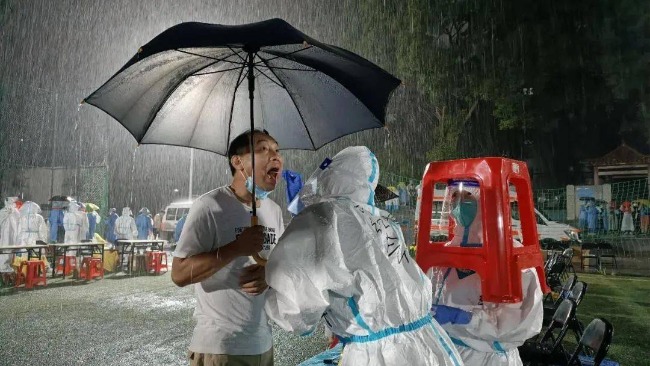 广州暴雨市民撑伞连夜测核酸 医护人员用高脚凳躲雨