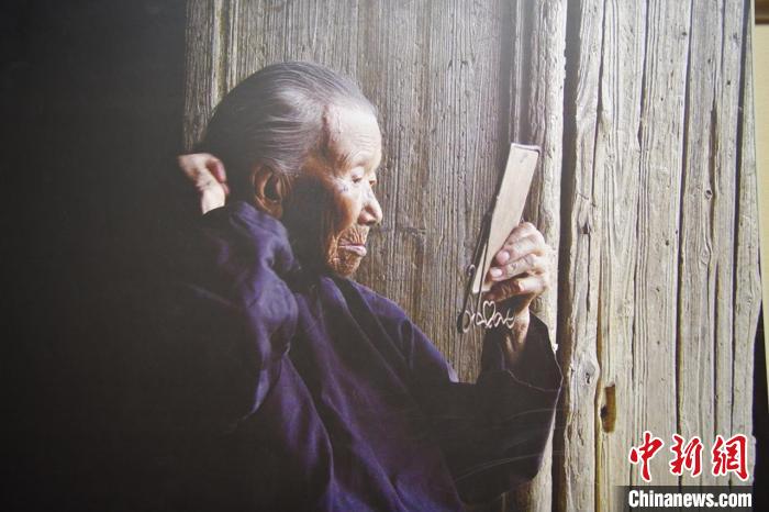 池煜华对着老镜子在百年老屋前梳妆。　兴国县委宣传部供图