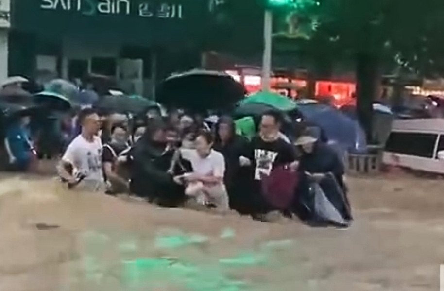 (郑州市民在暴雨中相互扶持涉水行走。图源正观新闻)