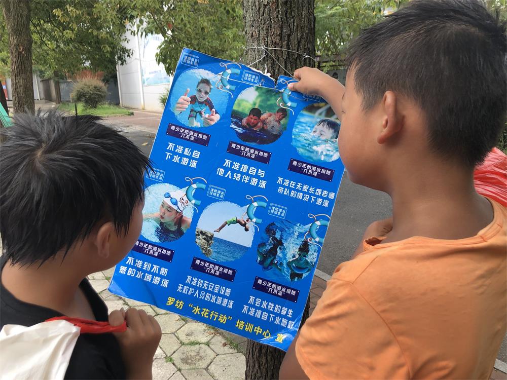 7月27日，罗坊镇希望小学，结束游泳考试后，两个学生正在看防溺水教育宣传牌。新京报记者 杜寒三 摄