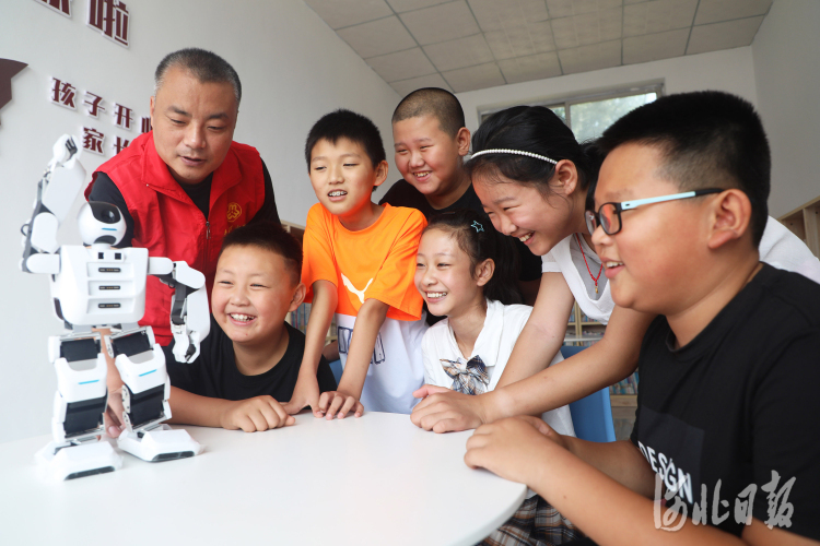 2021年8月13日，在河北省唐山市丰润区姜家营乡姜家营村，志愿者和孩子们一起观看机器人表演。