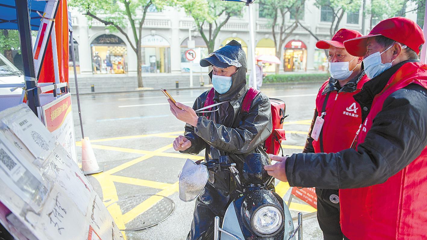 10月20日,在武汉市武昌区水果湖街道放鹰台社区入口,社区志愿服务队队员正在引导进出社区人员扫码测温。