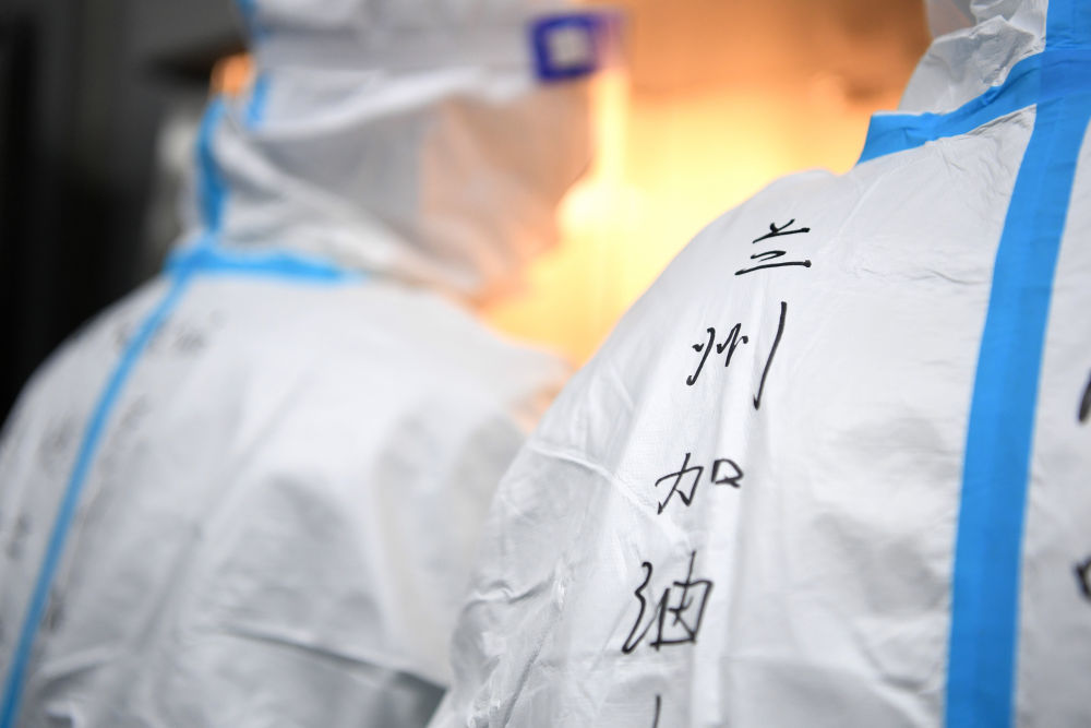 ↑10月21日，在中国铁路兰州局集团疾病预防控制所核酸检测实验室，检验师李鹏鸣的防护服上写着“兰州加油！”。