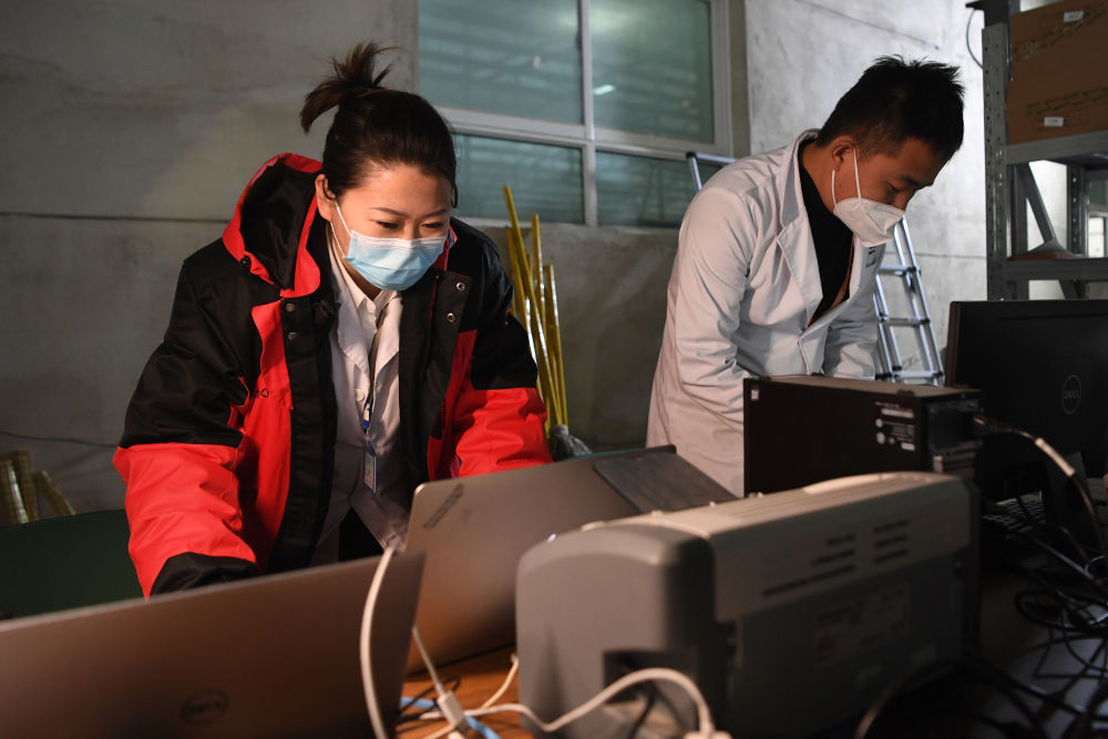 佟锦媚（左）和同事在“猎鹰号”硬气膜实验室外的耗材区用电脑查看防疫物资领取情况（10月26日摄）新华社记者 陈斌 摄