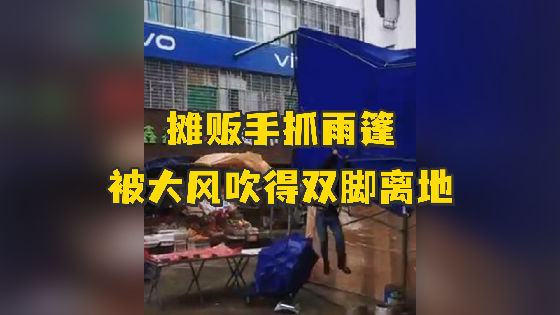 大风来袭，为保护雨篷，摊贩紧抓不放被大风吹得双脚离地