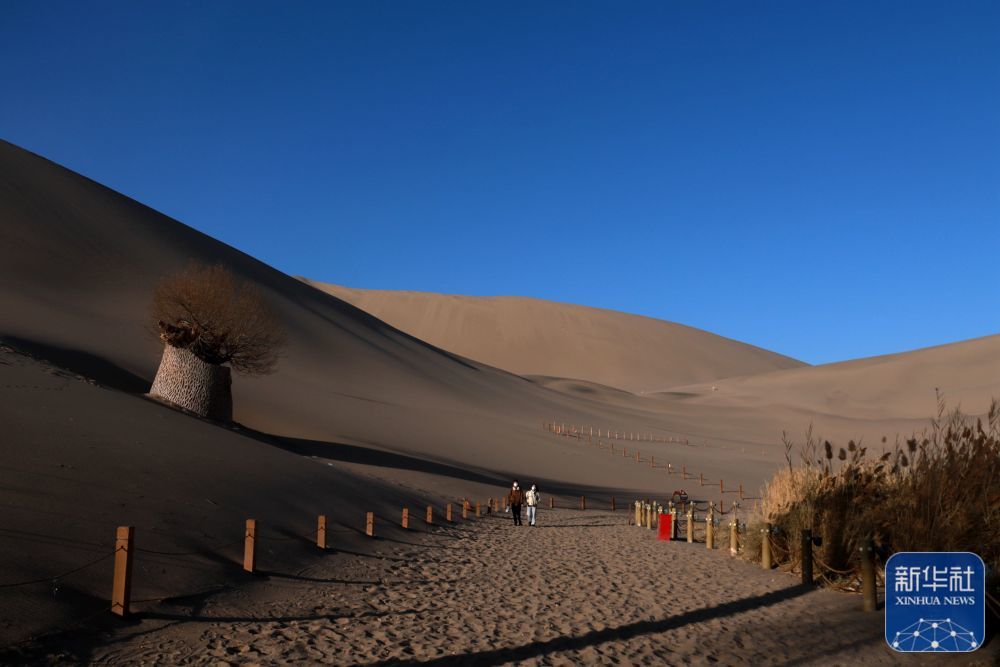 ↑11月27日，游客在甘肃省敦煌市鸣沙山月牙泉景区游览。