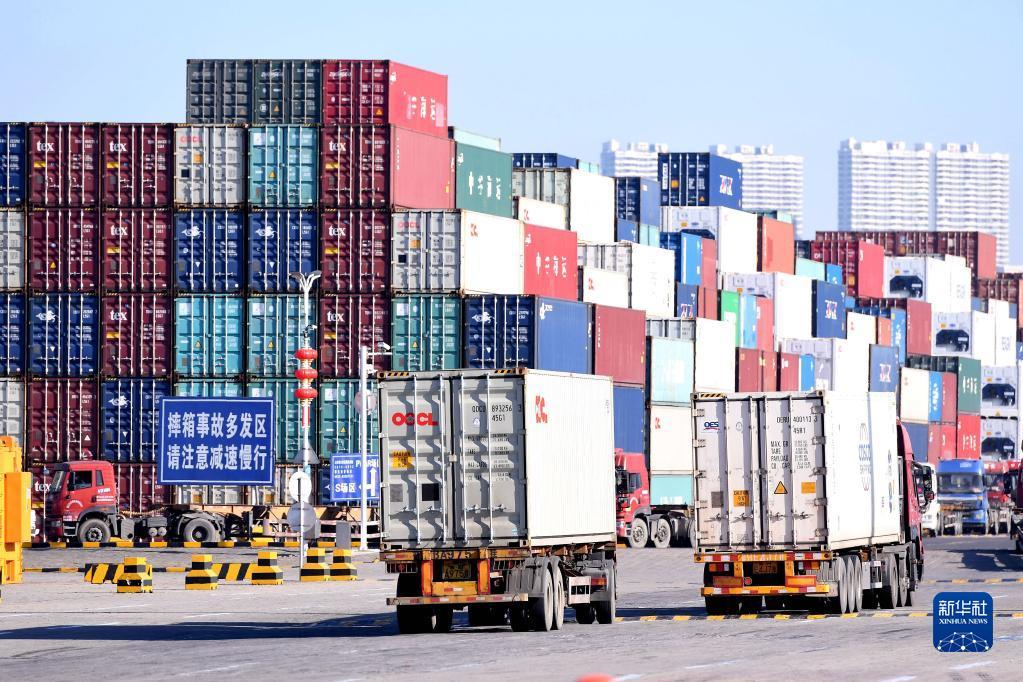 12月7日，在山东港口青岛港，运输集装箱车辆从堆积的集装箱旁经过。新华社发（俞方平摄）