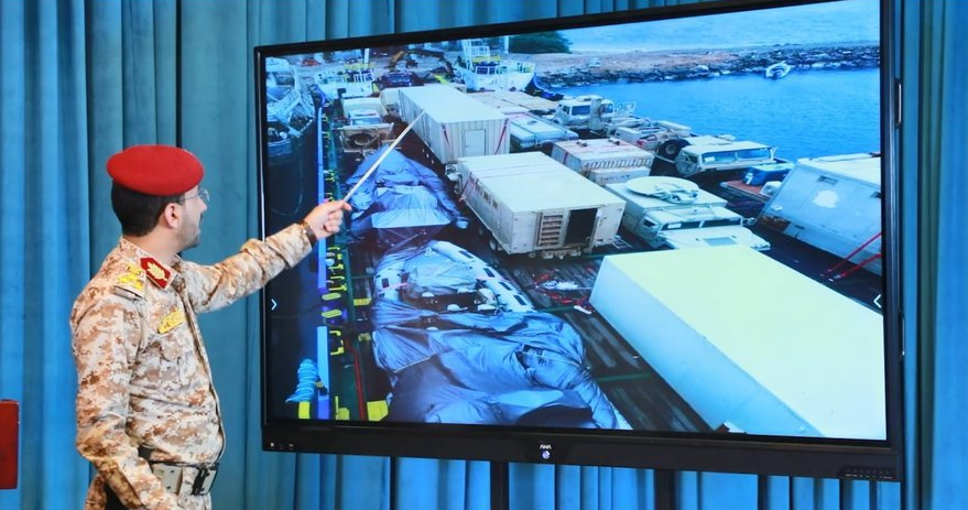 在新闻发布会上的叶海亚将军正根据无人机传来的画面讲解船上缴获物资的情况