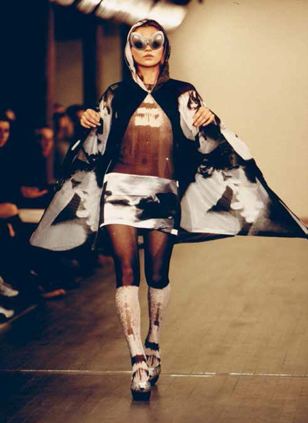 Stephen Sprouse 1998春夏系列的秀场，模特身穿一件安迪·沃霍尔作品印花的连帽斗篷，搭配同系列的短裙、半透明上衣和墨镜，1997年秋，纽约