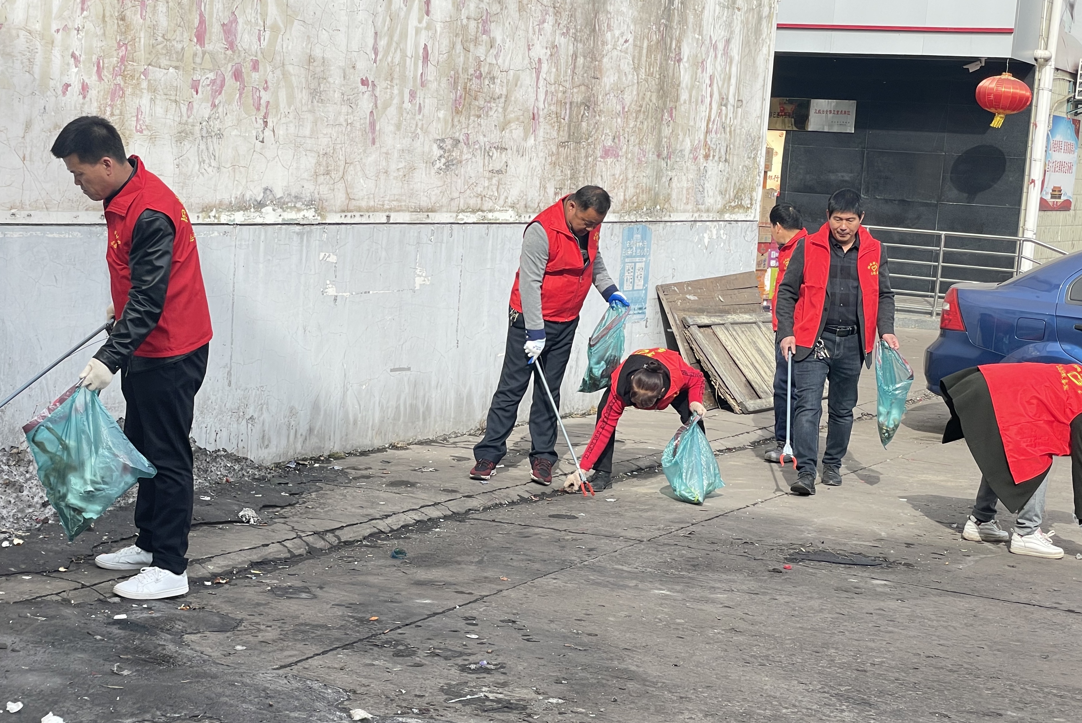 在崔家沟监狱辖区,志愿者们身穿红马甲,手拿清洁工具对社区道路两旁