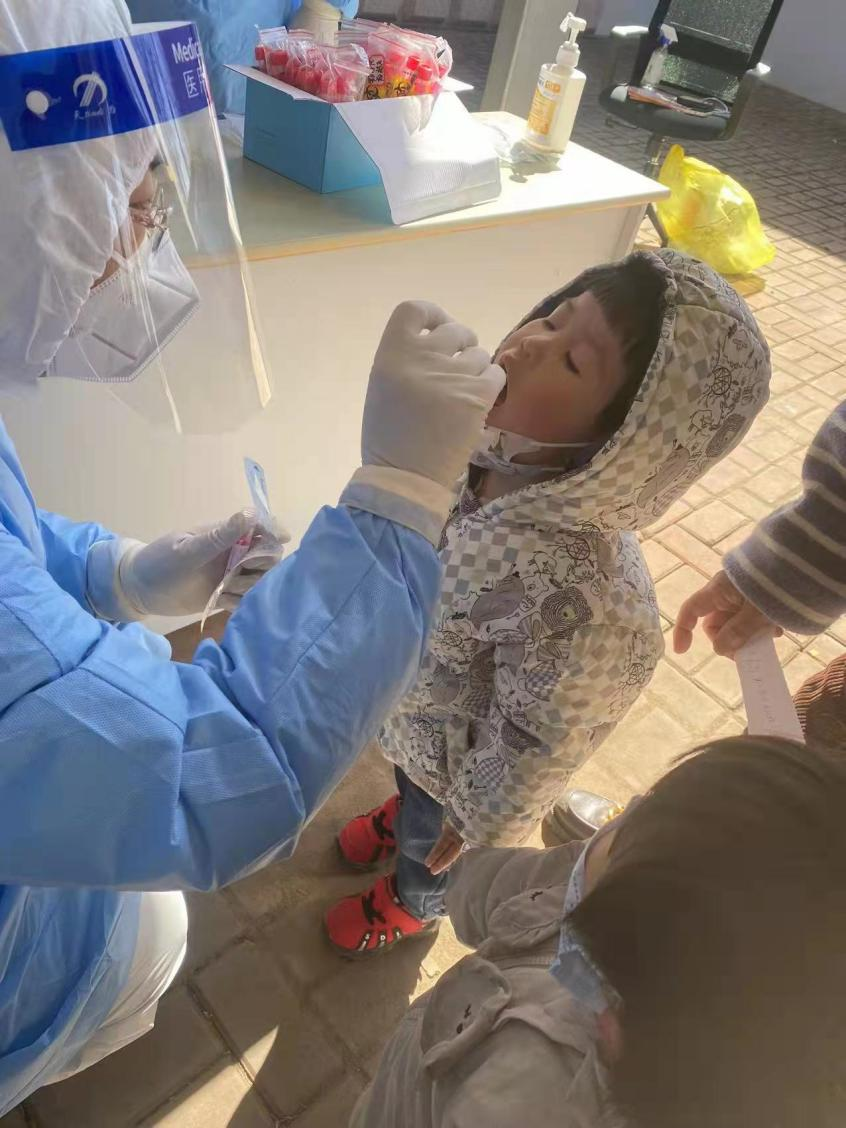 （图为莱西市夏格庄中心卫生院的护士潘颖超半蹲半跪为孩子们做核酸检测。）