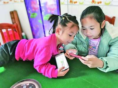 广西金秀县，两名儿童正在玩手机。何鲜桂摄/光明图片