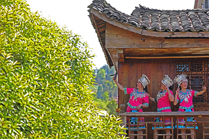 4月8日,游客身着苗族服装,在苗家吊脚楼上拍照游玩,体验古苗寨的独特