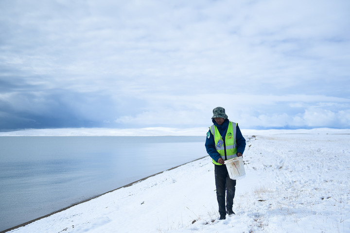 2021年10月，三江源国家公园黄河源园区生态管护员俄措在扎陵湖边捡拾垃圾。新华社记者张龙摄