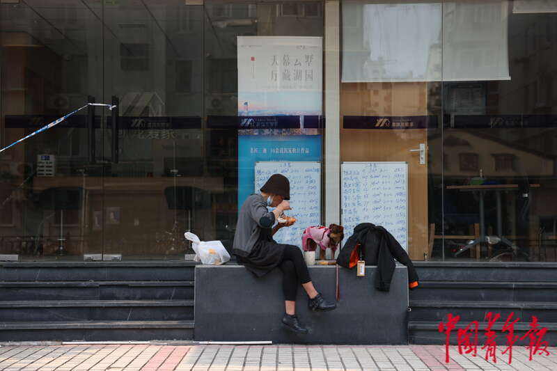 5月3日，上海市黄浦区，“电话亭女士”与她的狗“丽丽”正在一家暂停营业的房屋中介门前吃午饭。中青报·中青网记者 李强/摄