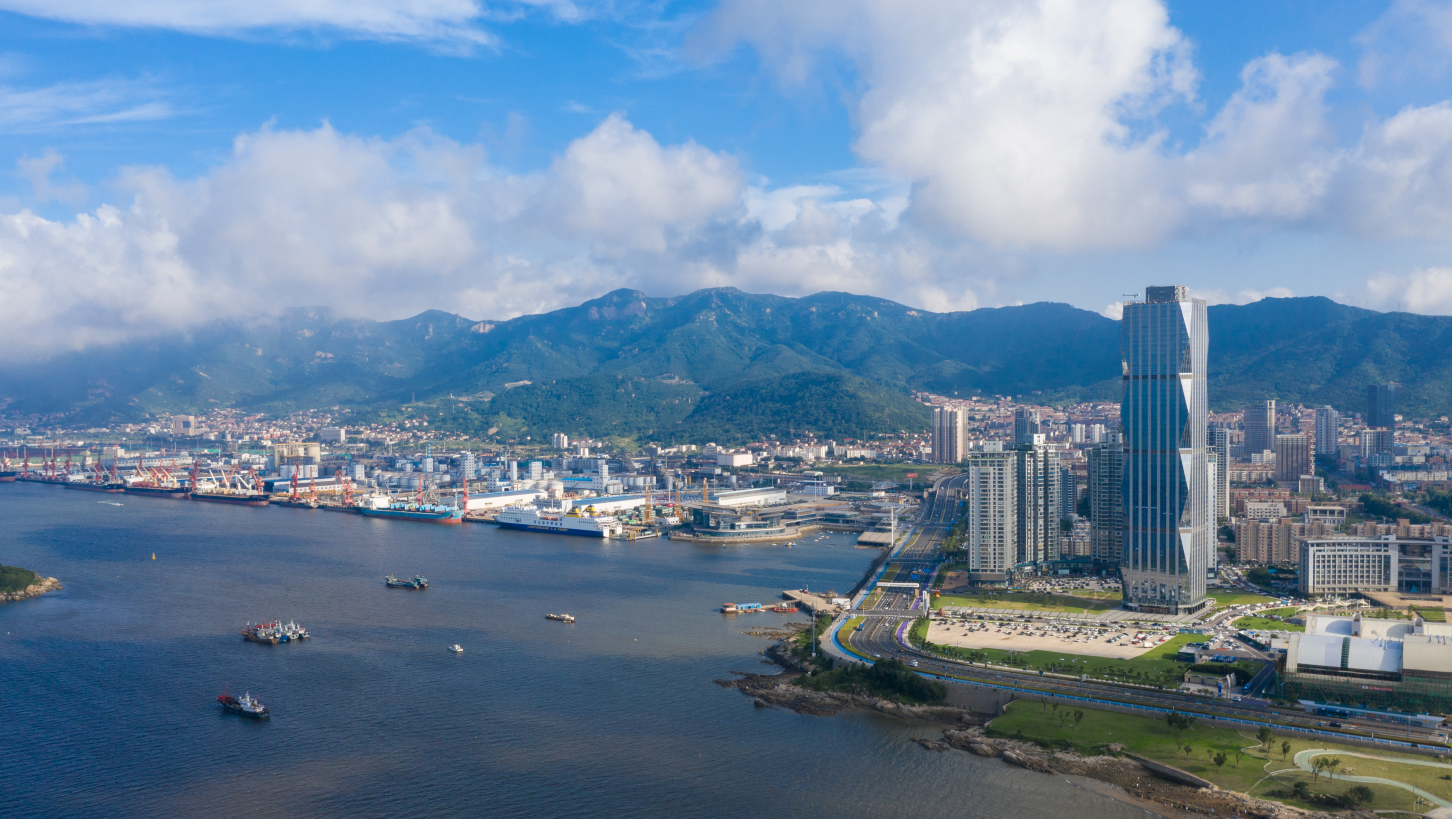 这是一张城市海港的航拍照片，显示了高楼大厦、港口设施、船只和远处的山脉，天空中有蓝天和云彩。