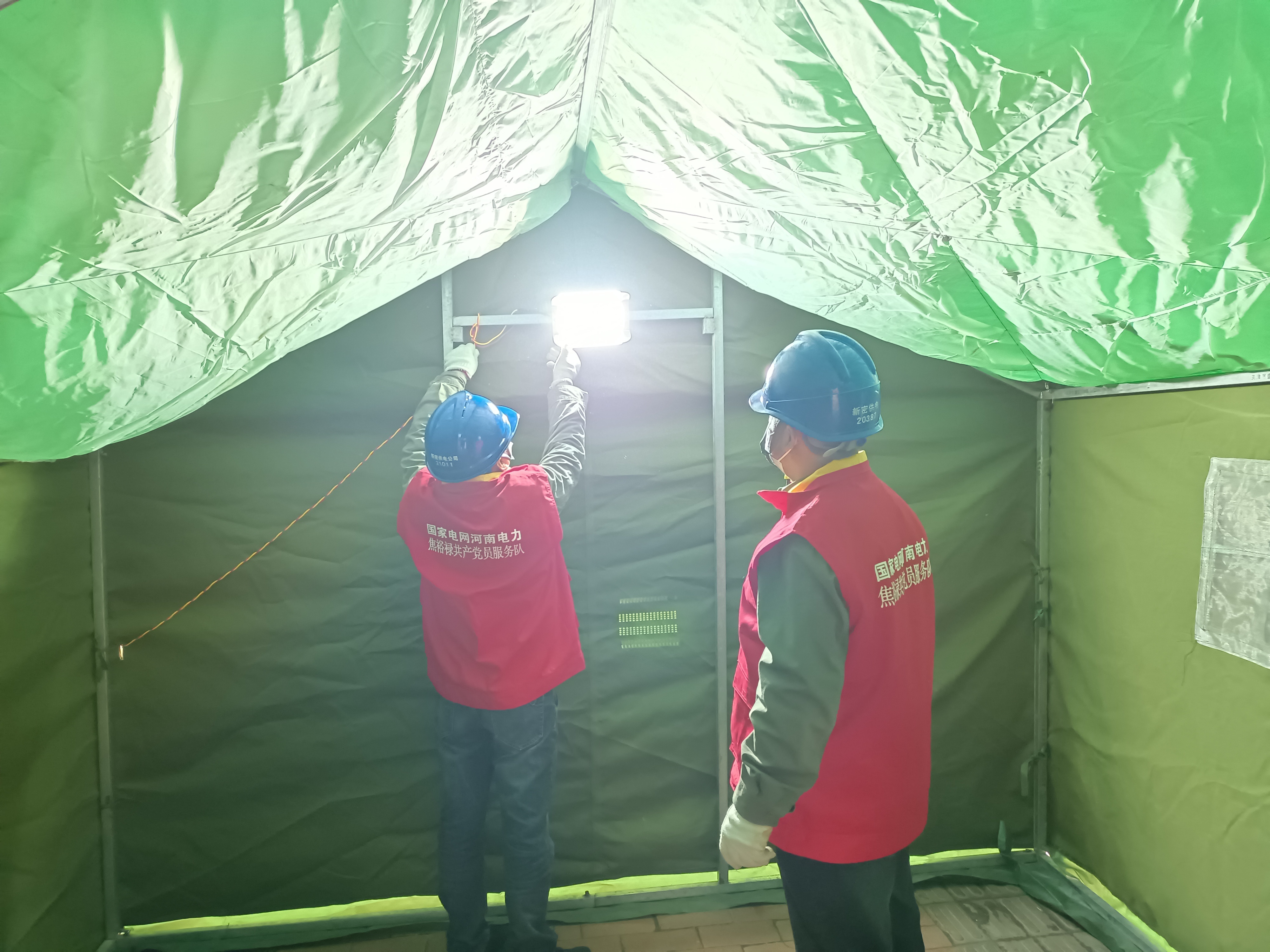 郑州新密市供电公司党员服务队队员为该市龙泉街核酸检测点帐篷搭设临时电源。（郭远辉）