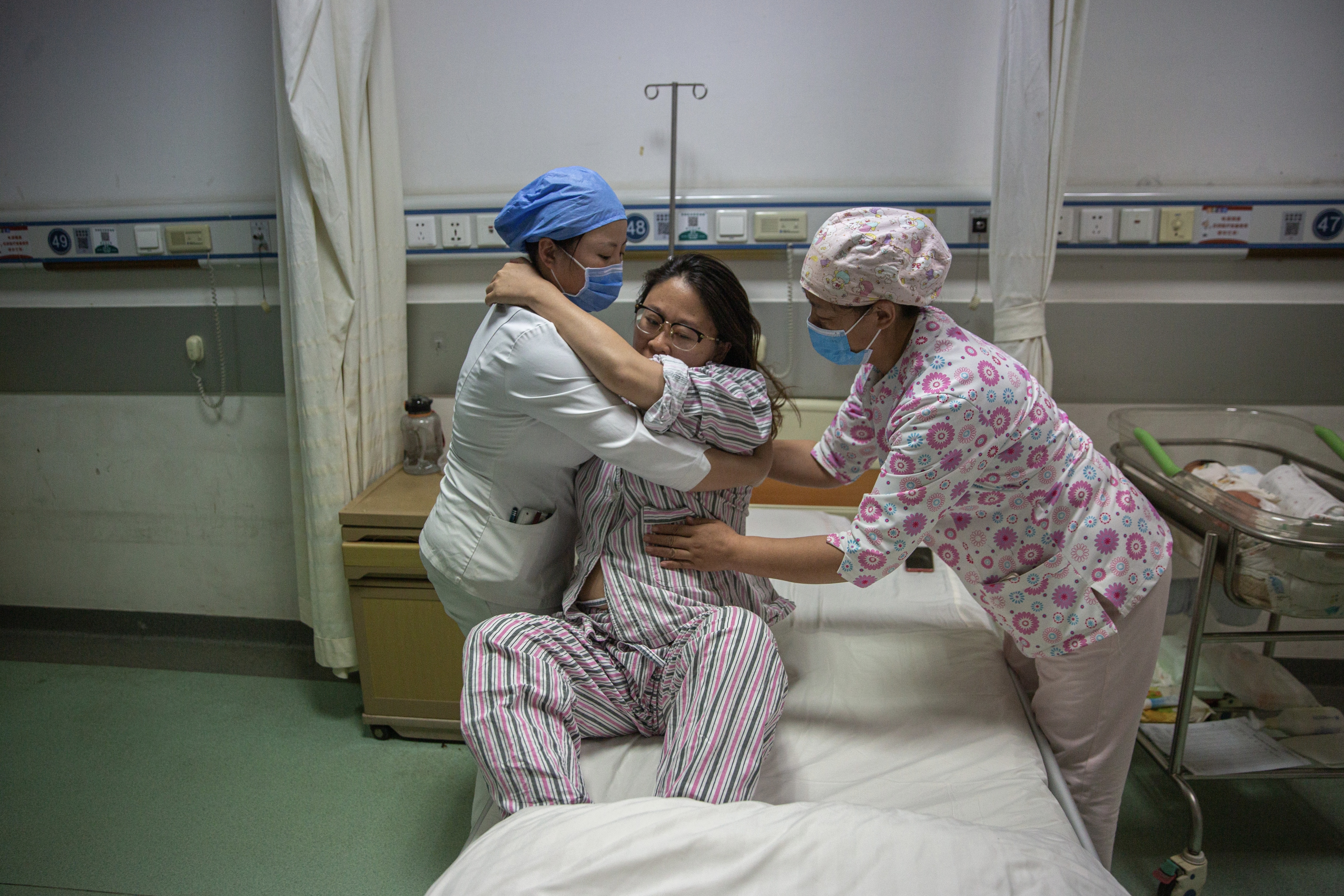 5月7日晚，北京大学首钢医院产科病房，护士闫玉琴与月嫂帮产妇温丹妮起身。