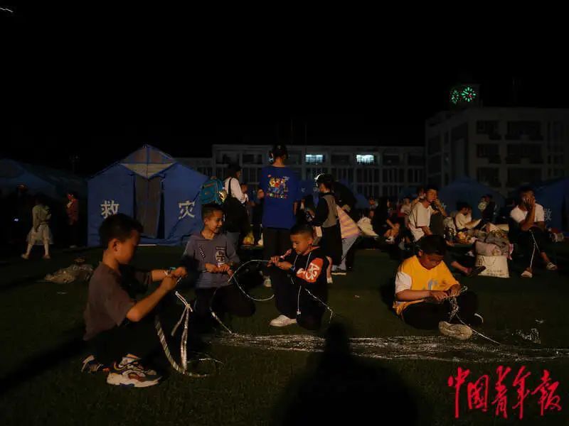 6月1日晚，四川雅安宝兴县七一初级中学体育场安置点，几名小朋友正在帮忙系塑料绳。程雪力/摄