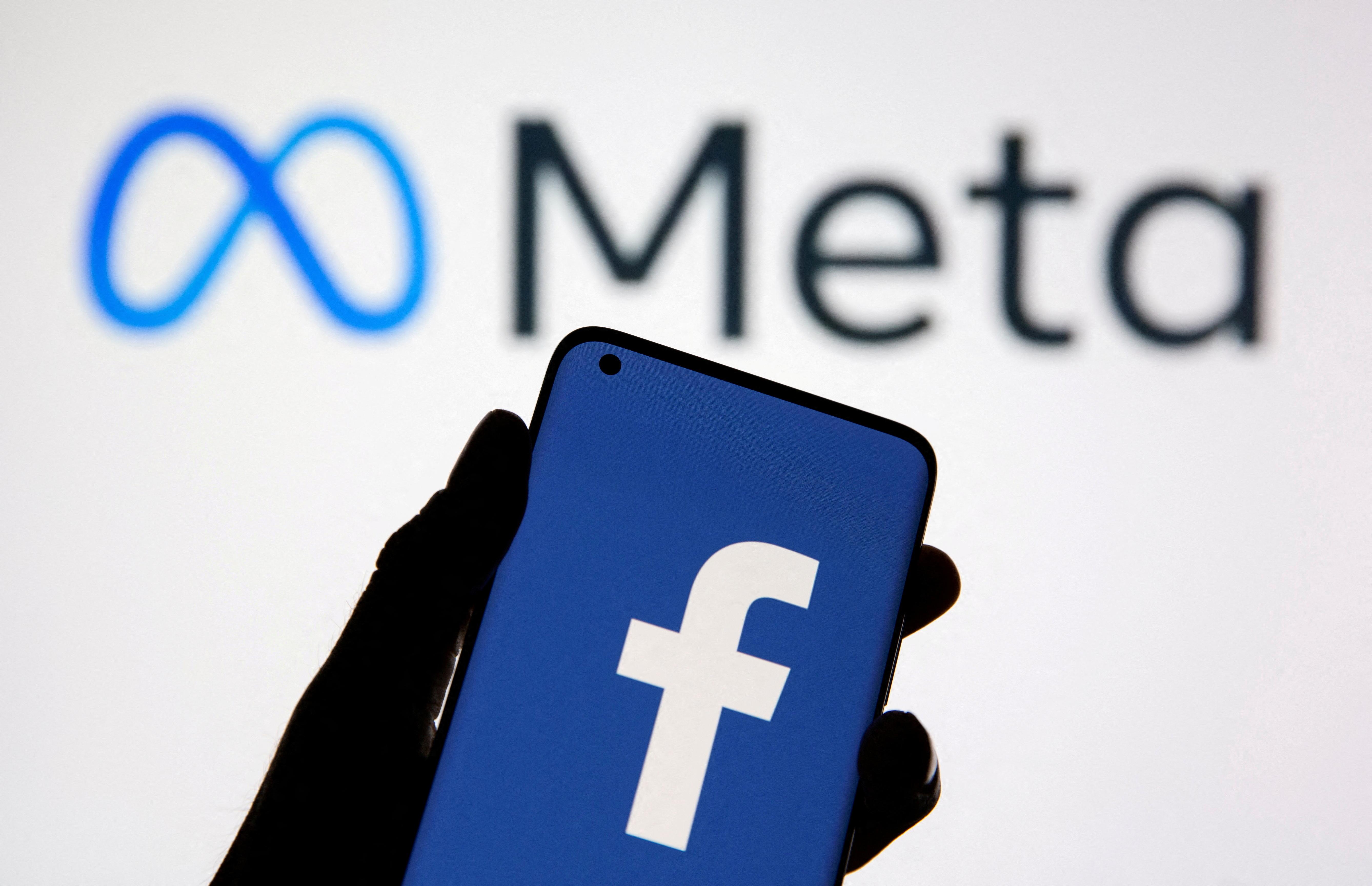 在此插图中，可以看到带有 Facebook 徽标的智能手机出现在 Facebook 的新品牌重塑徽标 Meta 前面