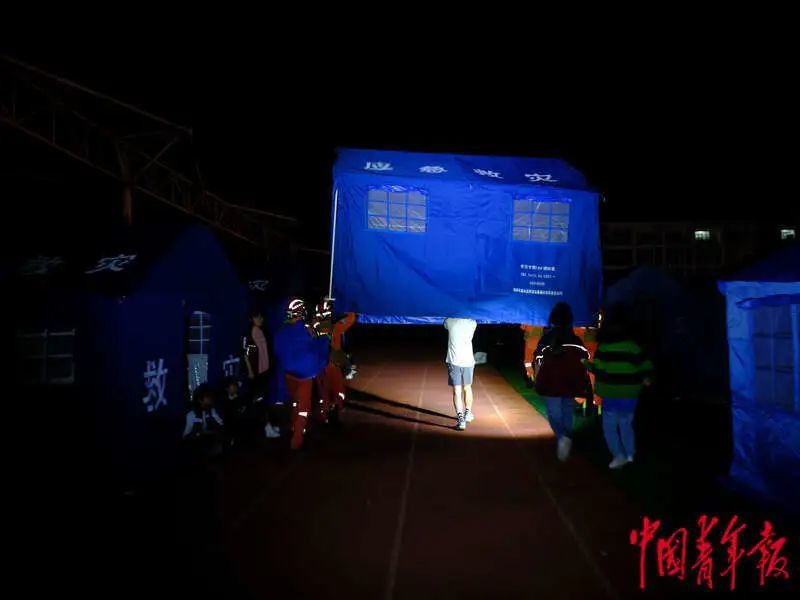 6月1日晚，四川雅安宝兴县七一初级中学体育场安置点，消防员与当地群众一同运送一顶搭好的帐篷。程雪力/摄