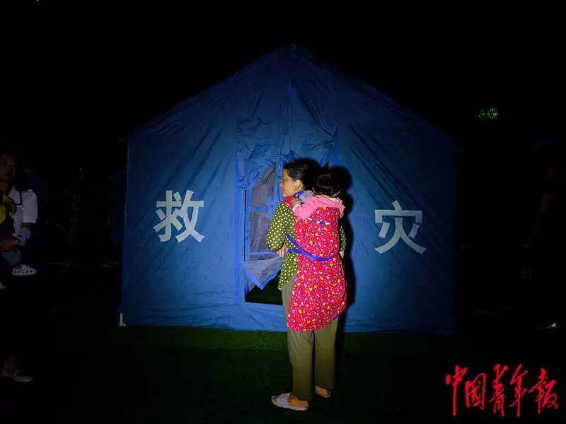 6月1日晚，四川雅安宝兴县七一初级中学体育场安置点，一名背着孩子的妇女在帐篷外停留。程雪力/摄