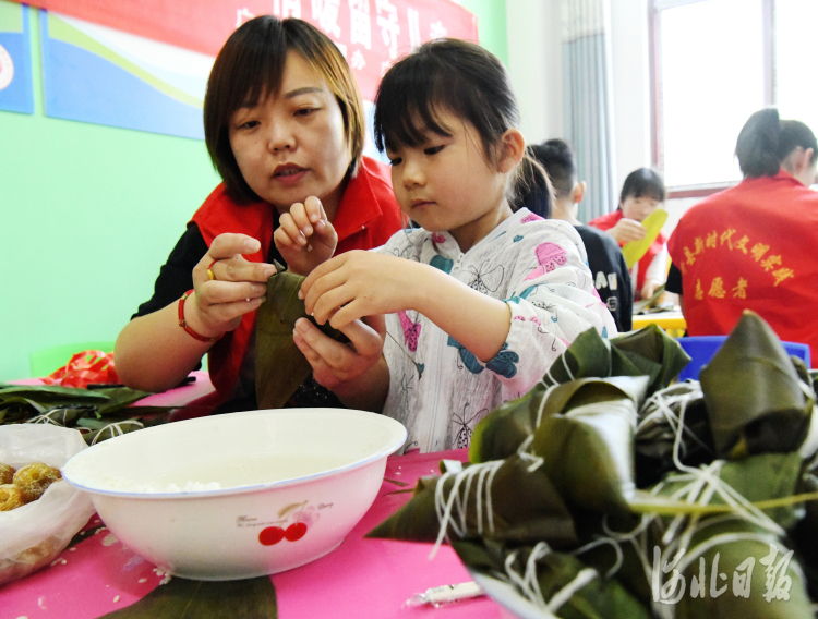 2022年5月28日，在河北省邯郸市广平县南韩村镇唐庄村，志愿者们在陪留守儿童一起包粽子。