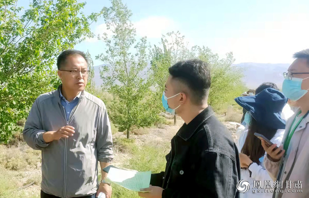 山丹县林草局林草资源综合管理中心主任牛登礼(左一)向采访团成员介绍荒滩滴灌造林情况 马斌 摄