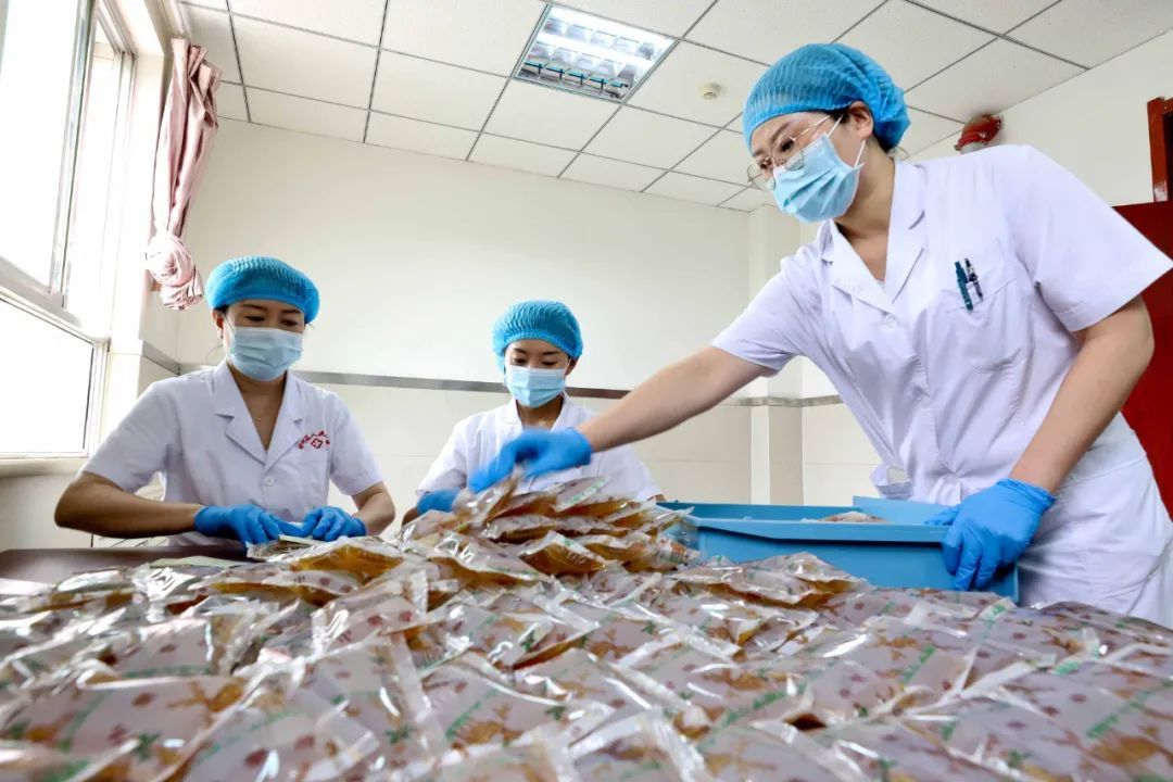 7月14日，张掖市甘州区人民医院中药汤剂煎配室的工作人员正在给煎配好的“岐黄清暑避瘟方”中药汤剂药袋上贴服用说明，准备送往各集中隔离点。