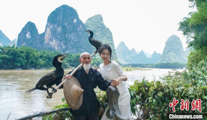 图为在桂林市阳朔县兴坪镇二十元人民币背景图案最佳摄影点，游客与黄月创合影。　欧惠兰 摄