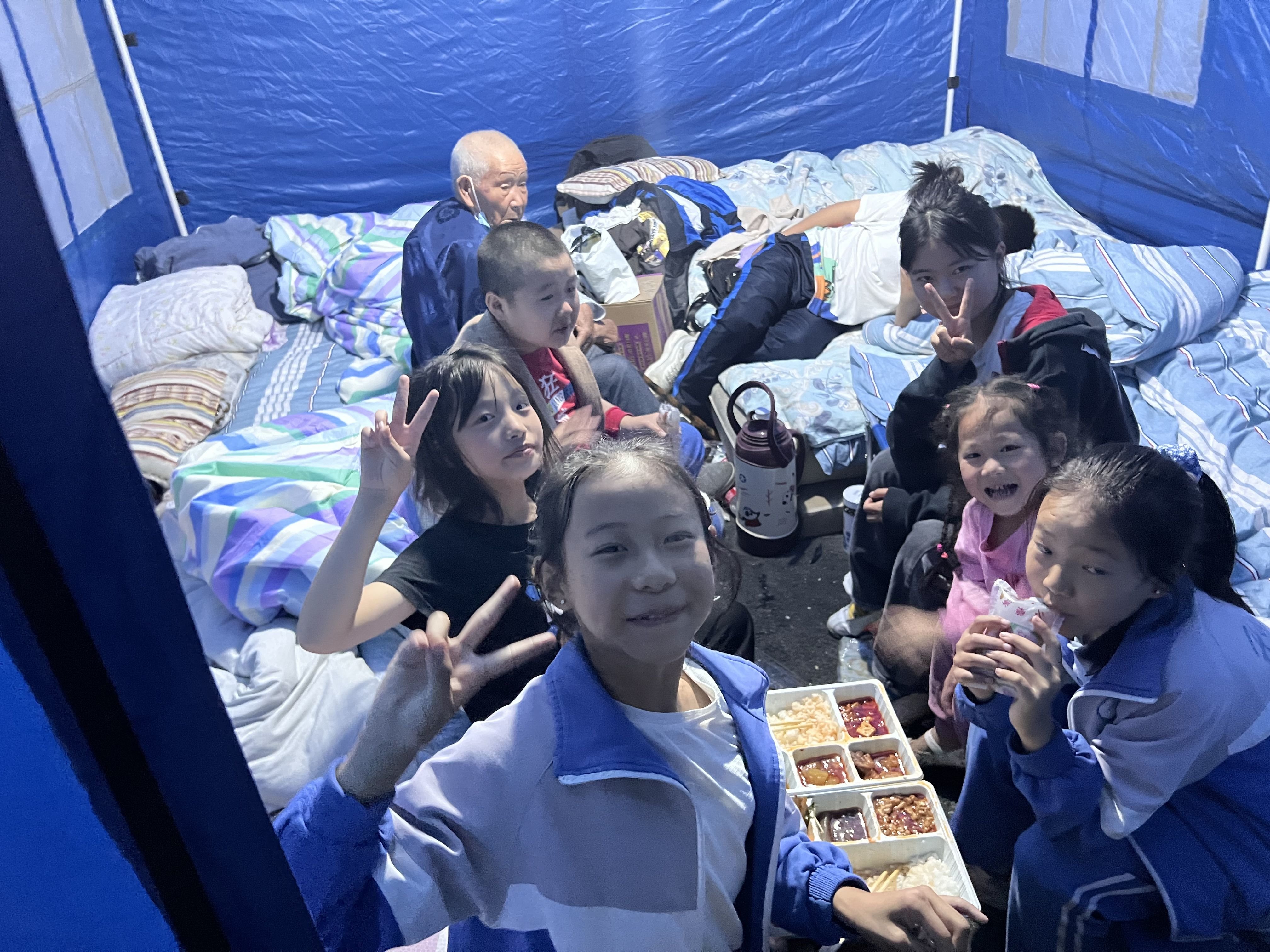 9月6日晚，夏新怡带着弟弟妹妹在磨西镇派出所安置点的救灾帐篷里吃晚饭。受访者供图