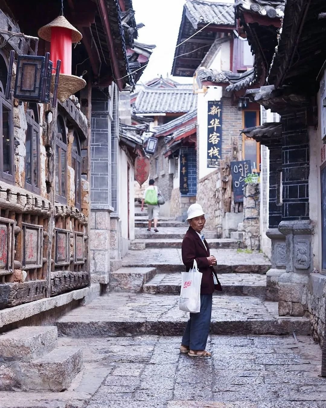 云南丽江 一位当地妇女走在鹅卵石铺成的街道上，两旁是古老的木制建筑© Lonely Planet / markread photography