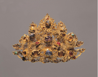 【镶宝石金帽饰&middot;明代&middot;兰州出土】帽饰分两层，底层以极细的金丝盘绕成繁密的涡状卷草纹；上层中间的金片錾刻出如意云纹，两侧各有一金凤，帽饰上镶缀各种宝石。
