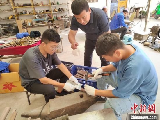 图为甘肃临夏州积石山县刀匠马尕主麻（中）教授年轻学徒锻打刀具（资料图）受访者供图