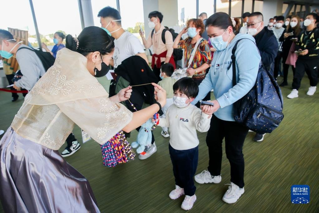 1月24日，在菲律宾马尼拉国际机场，礼宾人员在抵达大厅为中国游客戴上串珠项链。当天，菲律宾旅游部在现场安排了特色活动，热烈欢迎中国游客到来。新华社发（乌马利摄）