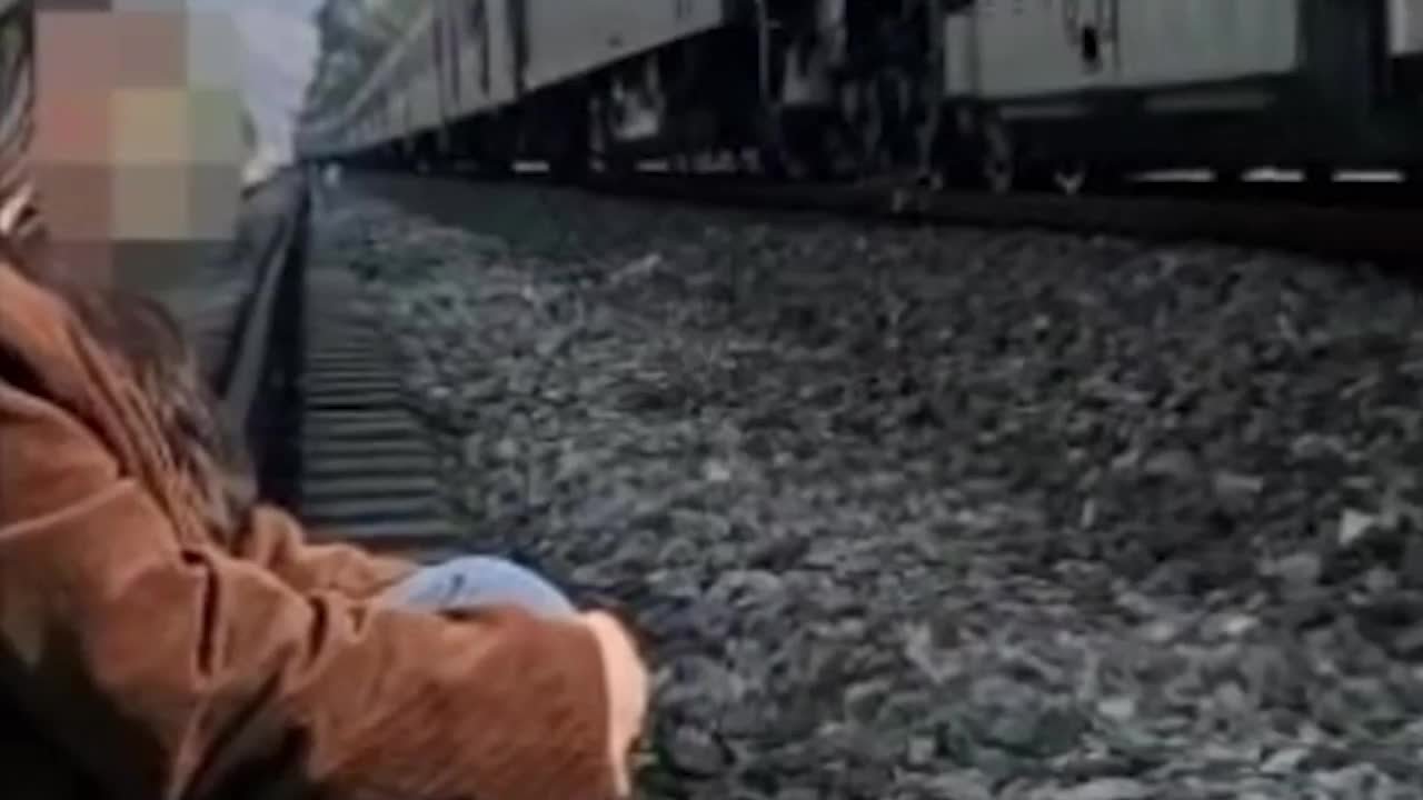 女子在铁路上淡定拍照，身后是一辆飞驰的火车