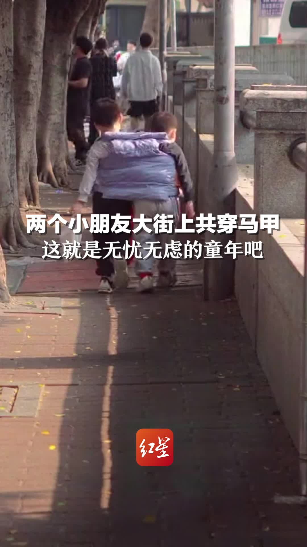 两个小朋友在大街上共穿一件马甲，这就是无忧无虑的童年吧