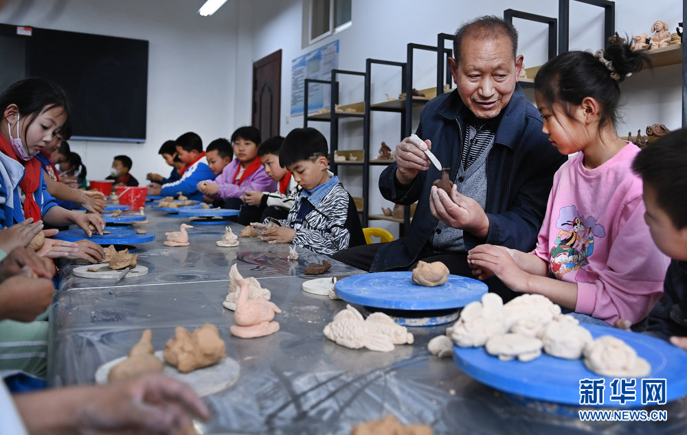 苗春生（右三）在指导小学生捏作泥塑作品。新华网发（林夕 摄）