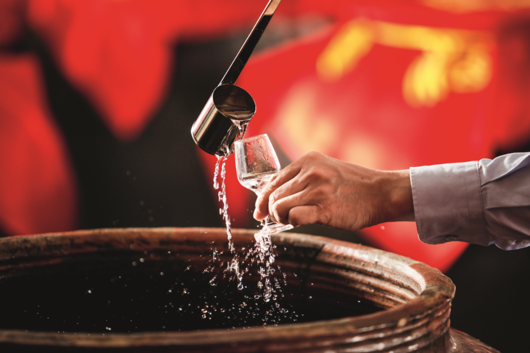 ▲ 酒厂工人从酒坛里舀出酒。 对材料、配方、工艺的一丝不苟，以及严格品控，保证每一瓶酒都是精品，成就独一无二的顺德美食美酒新名片。