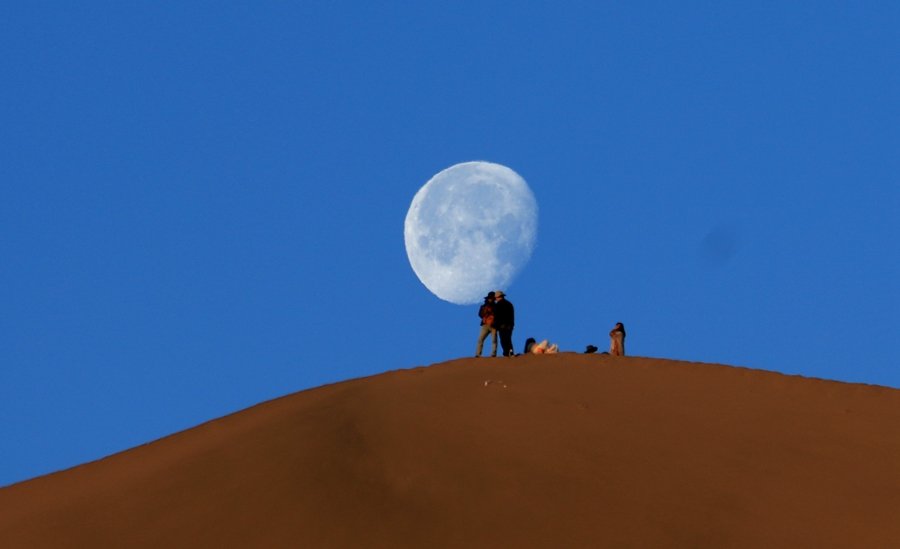 6月7日清晨，游客在甘肃省敦煌市鸣沙山山顶赏月。张晓亮摄