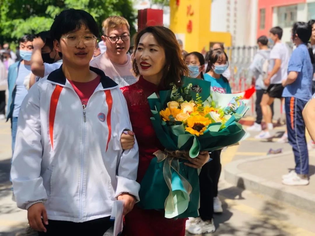 一位考生家长身着旗袍、手捧鲜花，为考生加油。