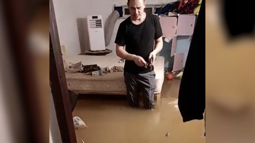 暴雨积水瞬间涌入家中，男子站在床边钓鱼